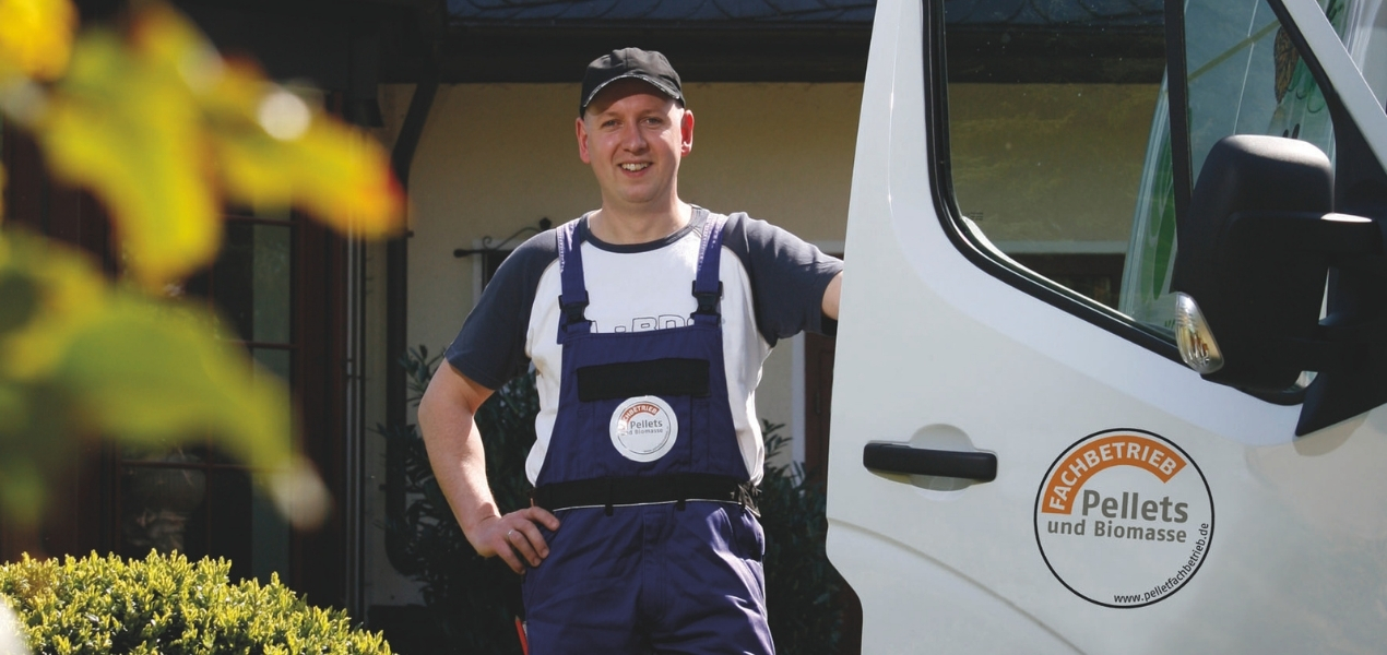 Handwerker steht neben dem Fahrzeug mit Blick zur Kamera