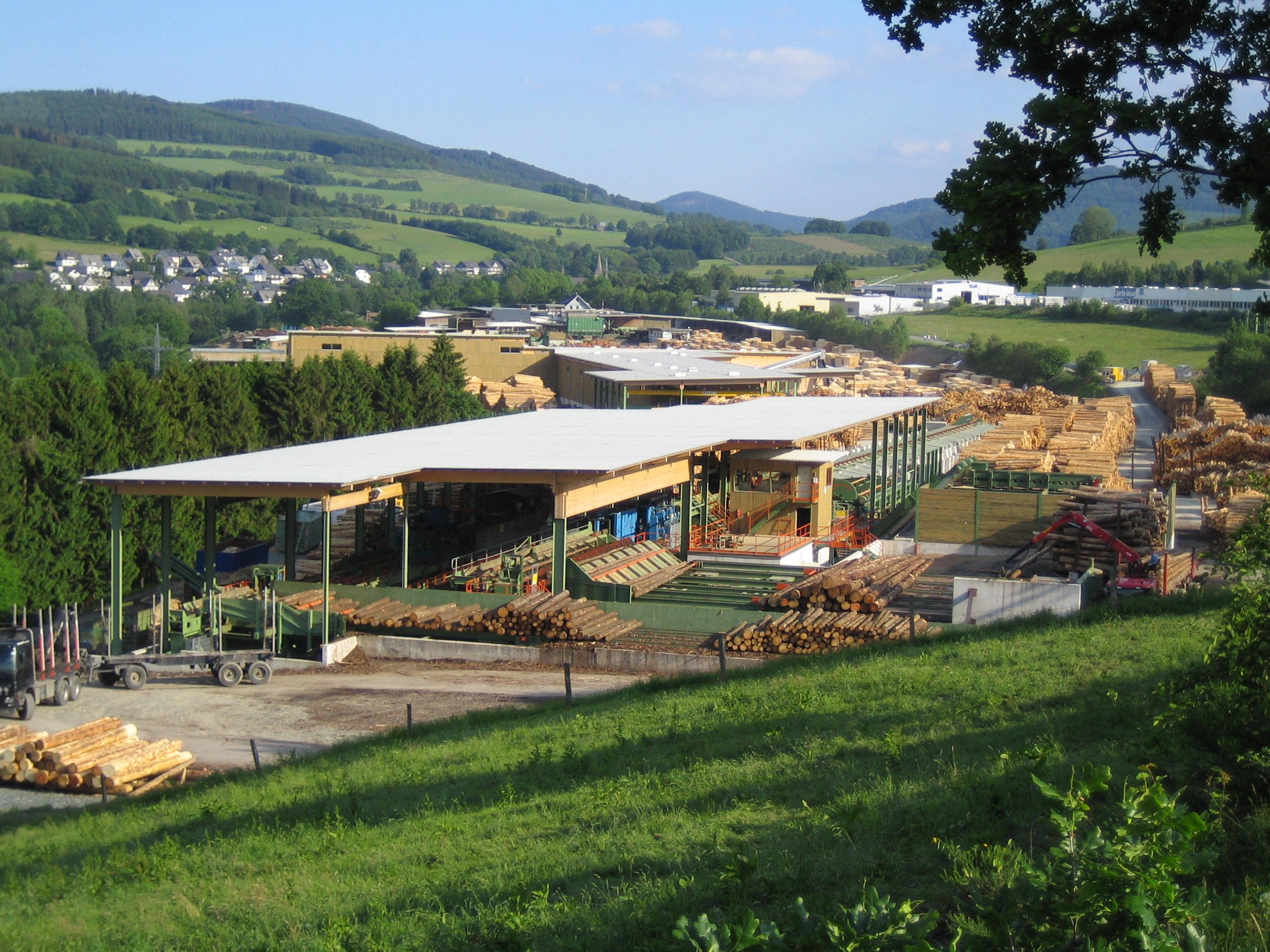 In der Mitte ist ein Pelletwerk umgeben von Hügeln und Häusern zu sehen. Oben ist ein blauer Himmel.