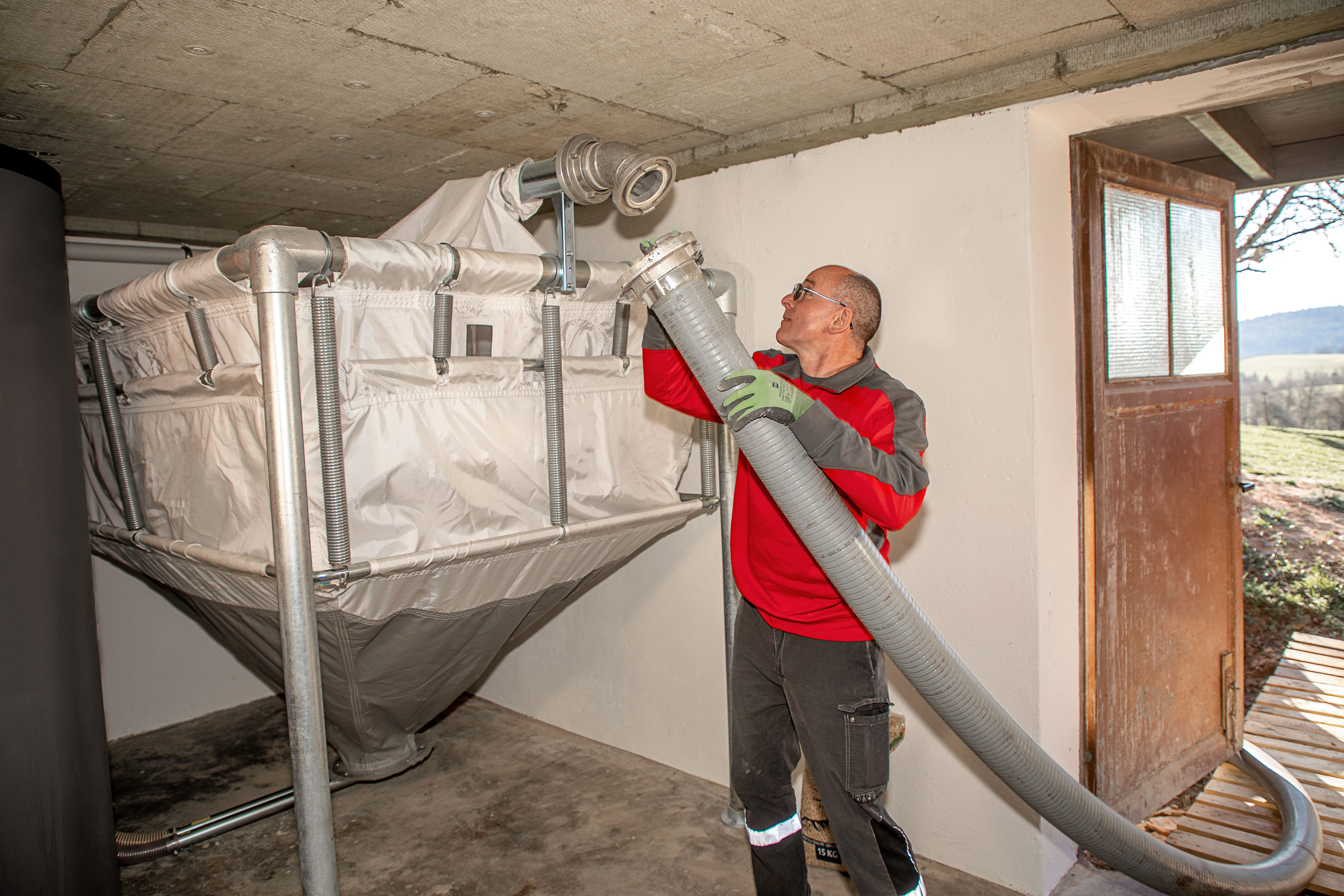 Auf dem Bild ist ein Pelletliferant mit Ausrüstung zu sehen, der ein Fertiglager mit konischer Form mit Pellets befühlt. Das Lager befindet sich in einem Kellerraum.