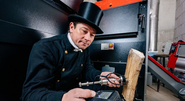 https://staging-media.depi.de/filer_public_thumbnails/filer_public/eb/1f/eb1f080f-757c-48dd-abbe-40f9a460e319/der-schornsteinfeger-kontrolliert-die-qualitat-des-holzscheites-fur-den-kombikessel-der-auch-mit-hackschnitzeln-beheizt-wird.jpg__640x350_q90_crop-smart_subsampling-2.jpg