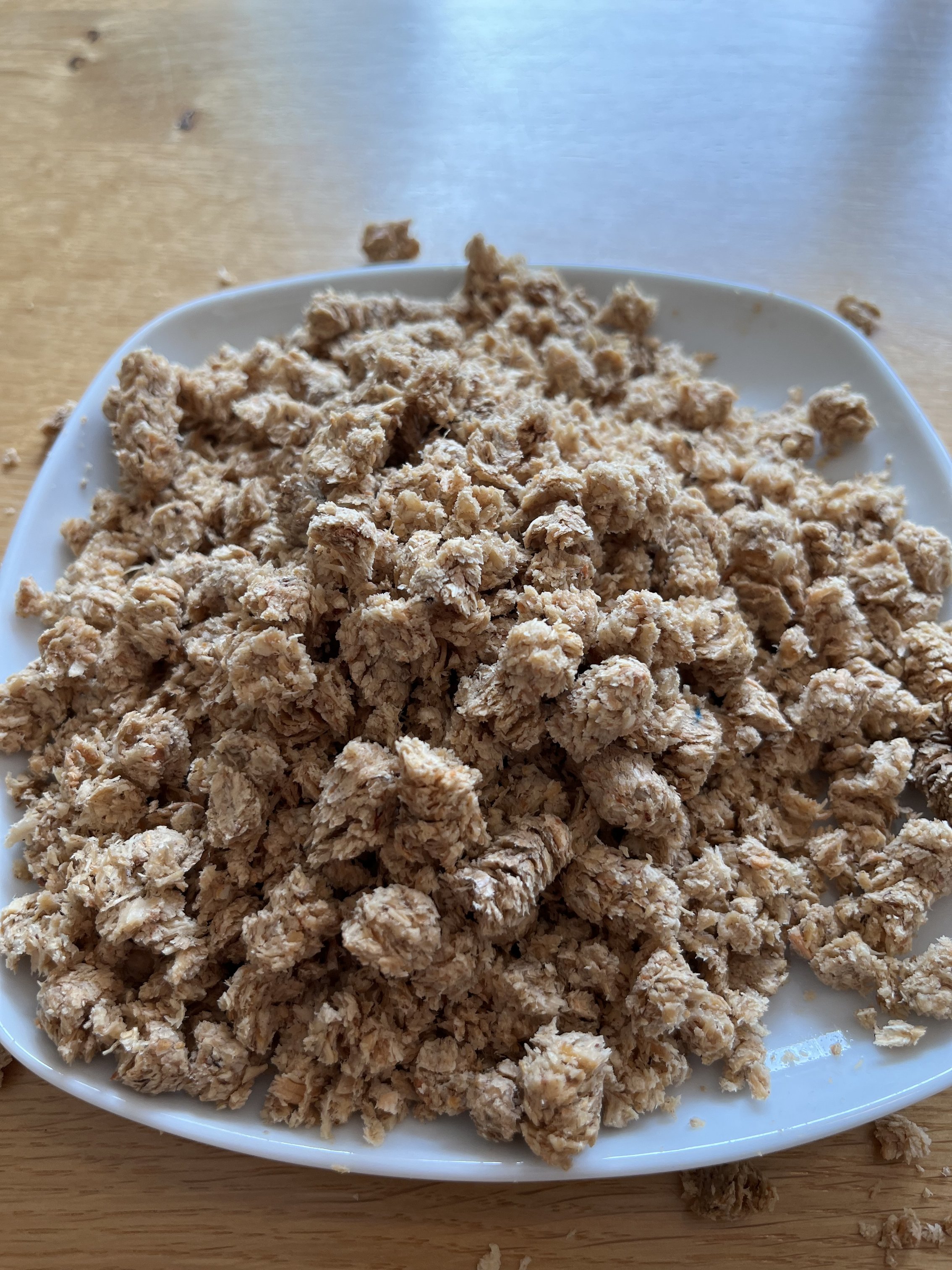 Auf dem Bild steht eine weiße flache Schale auf einem Holztisch mit nassen, aufgequollenen Pellets drin.